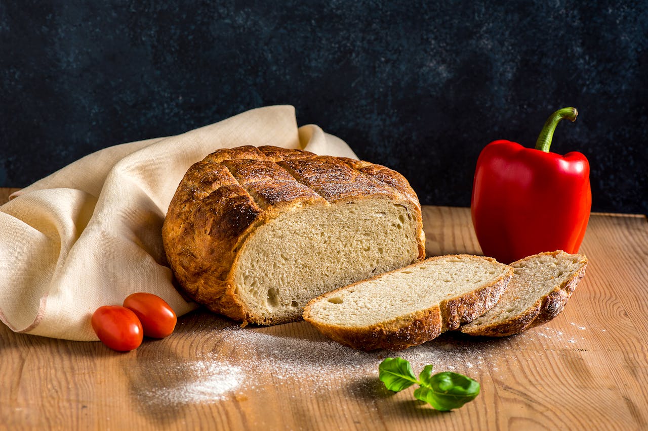 Delicious freshly baked sourdough bread with tomatoes and pepper on a rustic wooden table.